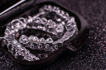 Transparent aligners spin in a black container. Plastic removable teeth correction retainers.