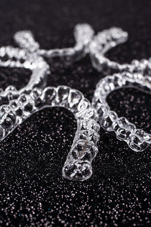Invisible aligner teeth retainers on a black background. Plastic braces dentistry retainers to...