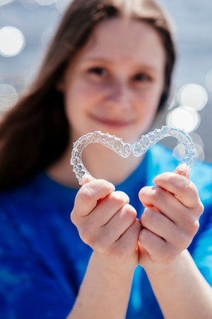 Dental care. Smiling girl holding heart-shaped aligners. Plastic retainers for teeth alignment.