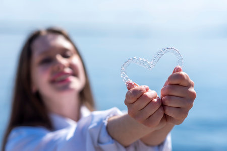 Dental care. Smiling woman holding heart-shaped aligners. Plastic retainers for teeth alignment.の写真素材