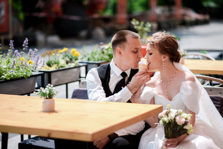 Happy bride and groom eating ice cream at a street cafe on their wedding day.の写真素材