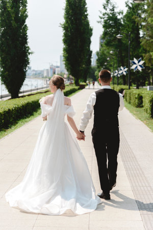 A happy bride and groom, holding hands, stroll through the city on their wedding day. The newlyweds, in love, take photos together.の写真素材