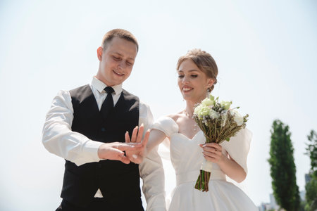 A happy bride and groom, holding hands, stroll through the city on their wedding day. The newlyweds, in love, take photos together.の写真素材