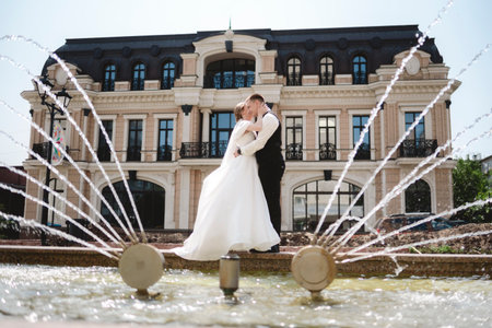 A happy bride and groom, holding hands, stroll through the city on their wedding day. The newlyweds, in love, take photos together.の写真素材