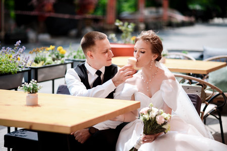 Happy bride and groom eating ice cream at a street cafe on their wedding day.の写真素材