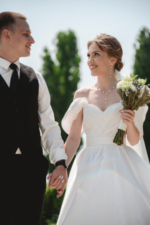 A happy bride and groom, holding hands, stroll through the city on their wedding day. The newlyweds, in love, take photos together.の写真素材