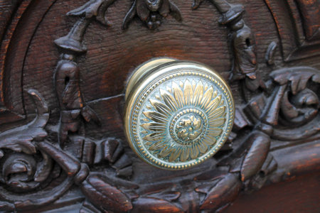 An ornate polished brass doorknob set in a heavily carved dark wood door in Paris, Franceの写真素材