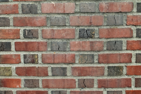 Weathered red brick wall with burnt, cracked bricks set in gray mortar