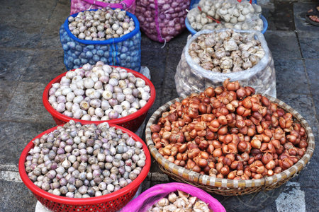 Baskets and bowls filled with onions, shallots and garlic cloves for sale at an outdoor market in Southeast Asiaの写真素材