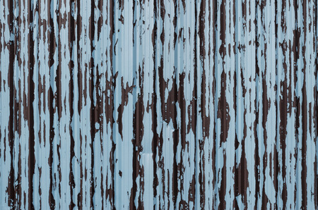 Corrugated steel fence panel with flaking and peeling paint in the colours of brown and pale blueの写真素材