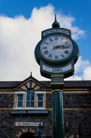 Betws y Coed, UK - Feb 2, 2019: A public time clock stands outside the main entrance to Betws y Coed railway Station in North Wales.のeditorial素材