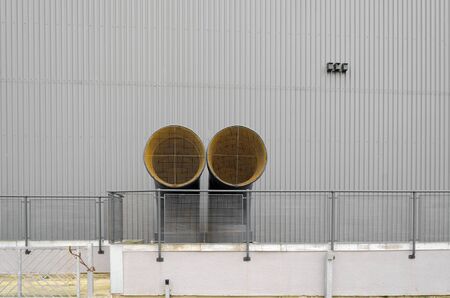A pair of air conditioning ventilation funnels. The yellow and black vent pipes are in front of a grey, modern, metal sheet covered building.の写真素材