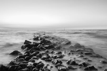A peaceful, black and white seascape. The tide creates a milky, dreamy scene as the sea swirls around a stone breakwater.の写真素材