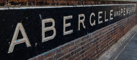 A metal sign built into a brick wall with the town names of Abergele and Pensarn.の写真素材