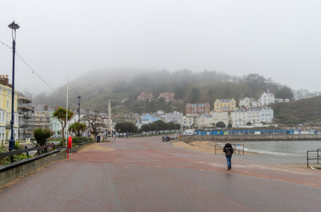 Llandudno, UK: Mar 18, 2021: People take their daily exercise along the promenade during the covid pandemic lockdown. Seen here on a grey, misty day.のeditorial素材