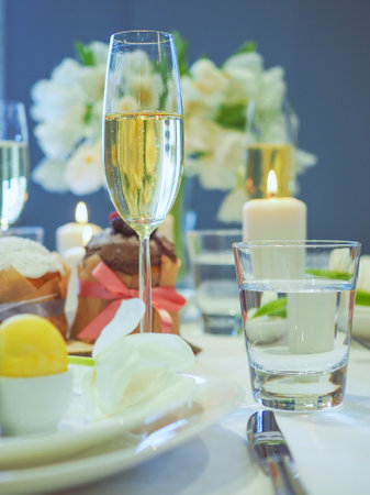 Serving a festive table for Easter, flowers, champagne glasses, eggs and cakes, candles serving,...