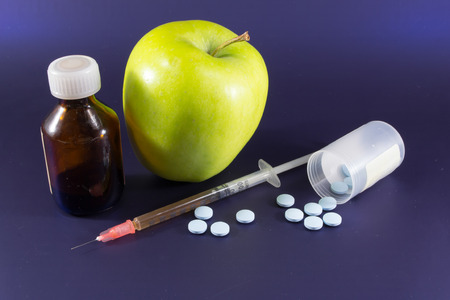 An uneaten golden apple with medicine pills and an unused hypodermic needleの写真素材