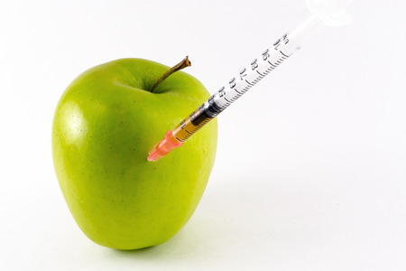 A hypodermic needle penetrates a fresh golden yellow apple in close upの写真素材