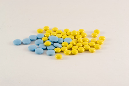 A pile of yellow and blue medicine pills and tablets with bottles isolated on white