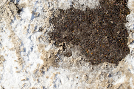 A car leaves tracks in the winter snow with concrete details underneathの写真素材