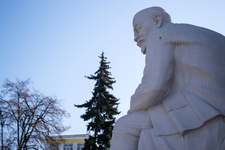 White stone statue of Lenin against a blue sky and pine trees