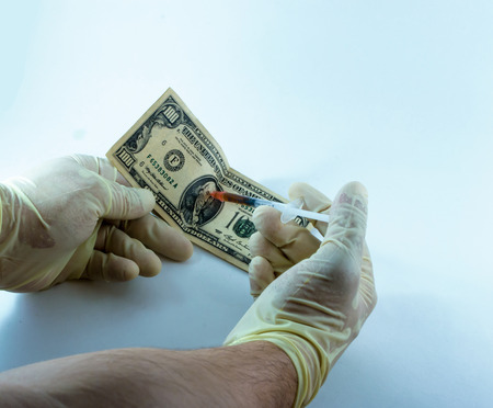 A latex gloved stranger injects a hundred dollar bill with a stimulant designed to grow the economyの写真素材