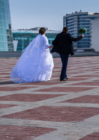 A married couple walk off into the city waving flowersの写真素材