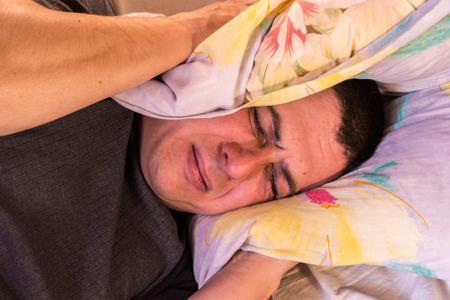 A man feels the effect of noisy neighbours as he tries to sleepの写真素材