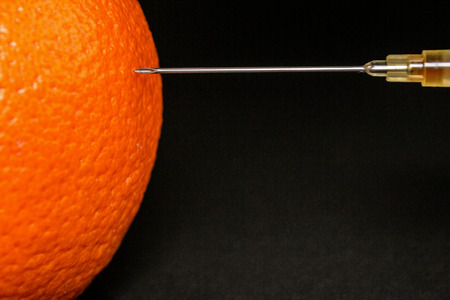 Medical needle starts to inject an orange with an unknown liquidの写真素材