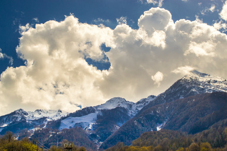 White clouds cast shadows on snow peaked mountainsの写真素材