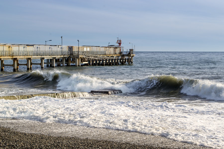 Seaside waves and a disused pier with a stone beach and grey skyの写真素材