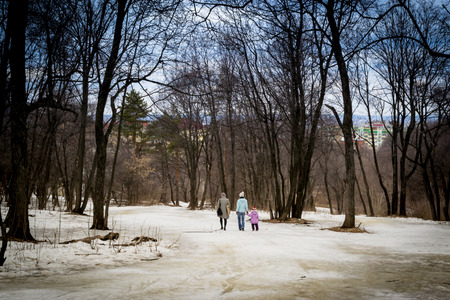 two women and a child walk in a winter forest with black treesの写真素材