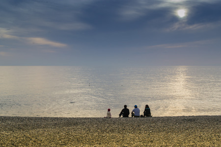 4 People gaze out at a calm sea as the sun begins to setの写真素材