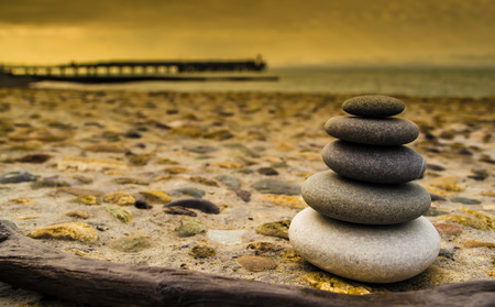 Balancing stones on a rough stone background with the sea and a pier in the distanceの写真素材