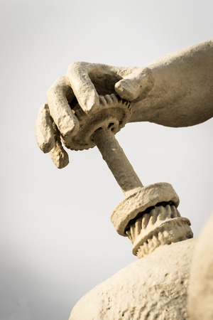 Human hand statue in white stone holding a industrial work cogの写真素材