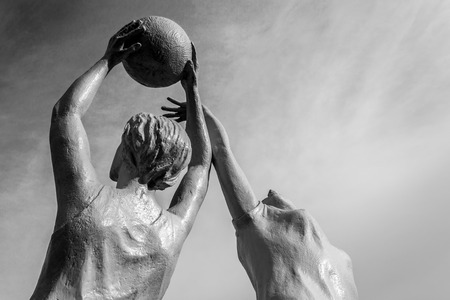 White stone statue of two women playing netball against a blue skyの写真素材