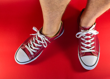 White male human legs and feet wearing a pair of red canvas trainers with backgroundの写真素材