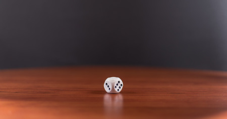 Single wite die on wood with black background showing the numbers three and six