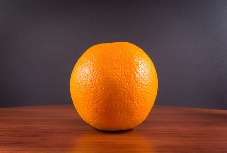 Single ripe orange on wooden rustic surface with grey black backgroundの写真素材