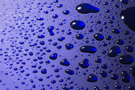 Clear water droplets reflected from bright blue metal with white copyspaceの写真素材