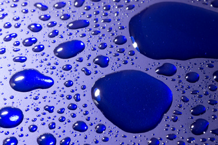 Pools of water droplets reflected from bright blue metal with white copyspaceの写真素材