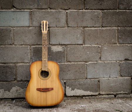 Single antique guitar resting against a grey brick wallの写真素材