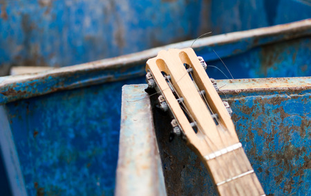 Old unwanted guitar thrown away in an rusty metal dumpsterの写真素材
