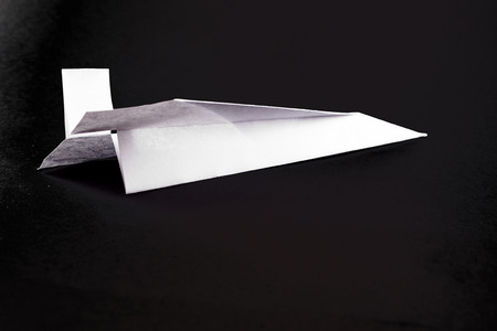 Solitary white paper airplane in flight on a black backgroundの写真素材