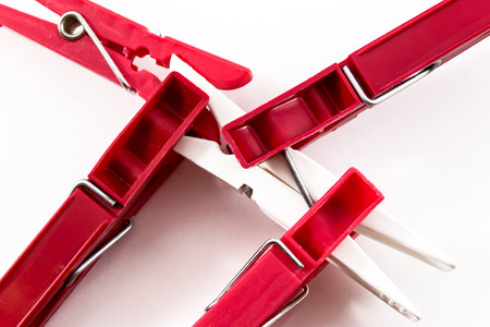 Four dark red plastic pegs overcoming a single solitary white plastic pegの写真素材