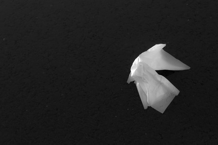 Thrown away peice of white paper absorbs water from a pond of rainwaterの写真素材