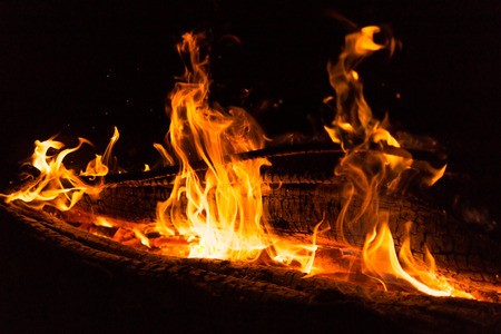 Bright golden color flames and embers from a campfire at nightの写真素材