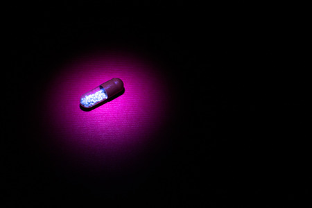 Single pill capsule with contents in light area amongst darkness on a maroon red backgroundの写真素材