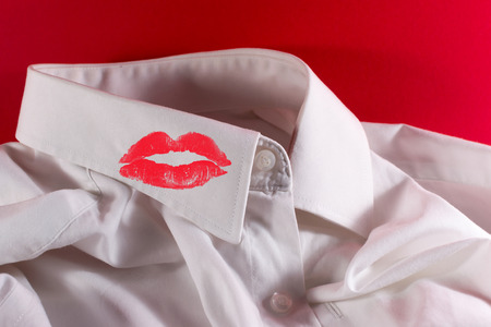White used shirt on a crimson background with woman's red lipstick on the collarの写真素材