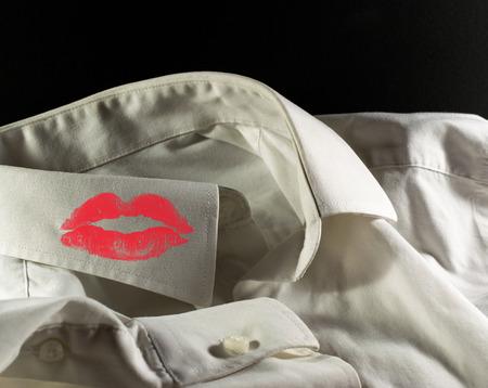 White used shirt on a black background with woman's red lipstick on the collarの写真素材